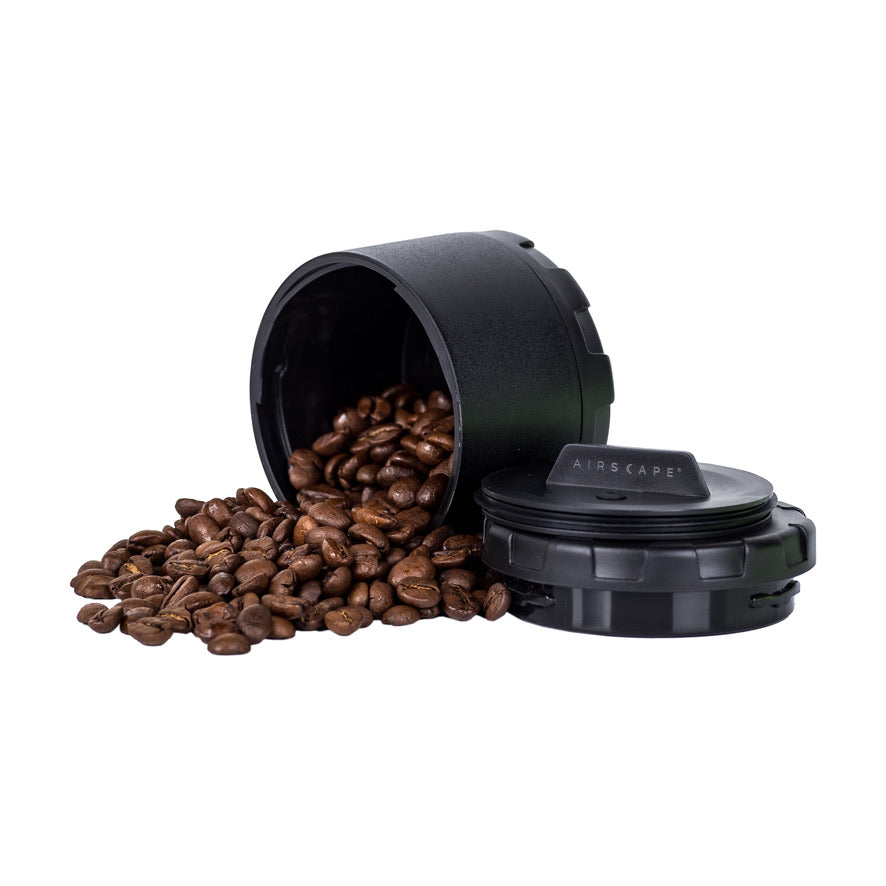 Black container with coffee beans spilling out on a white background