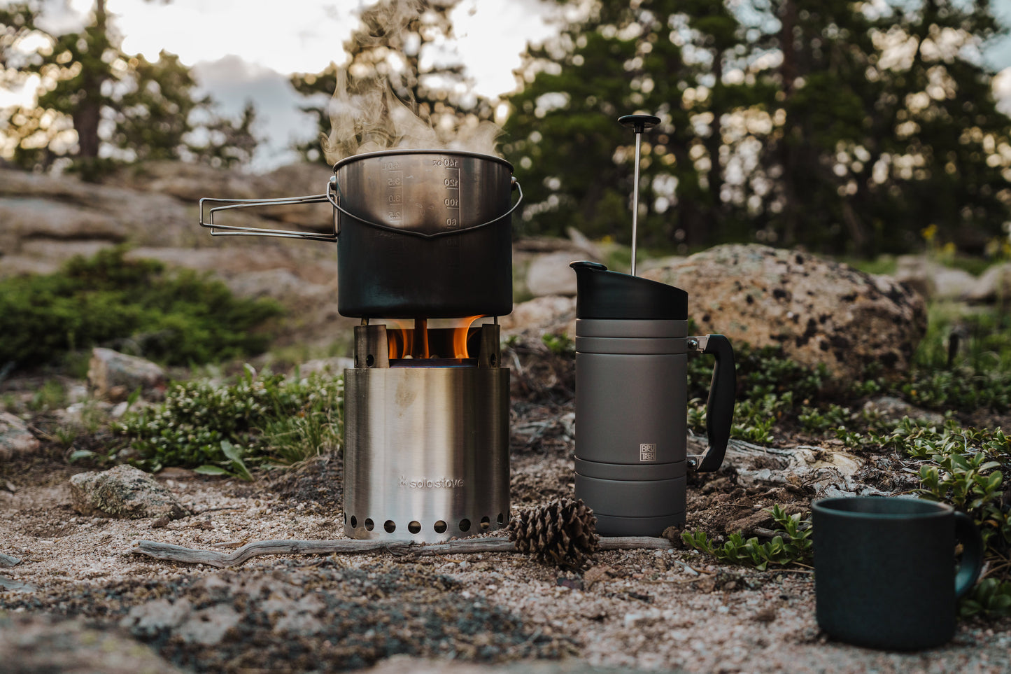 Camp stove with pot and insulated gray travel French Press on a natural outdoor setting