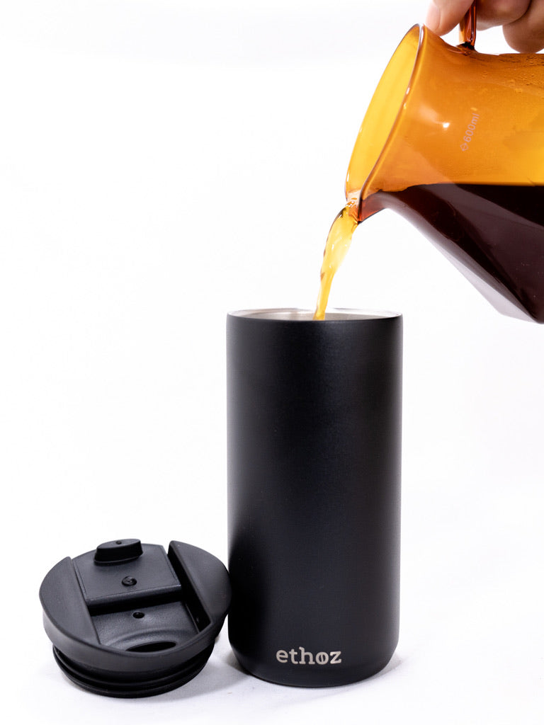 Black insulated tumbler with 'ethoz' branding being filled with a coffee.