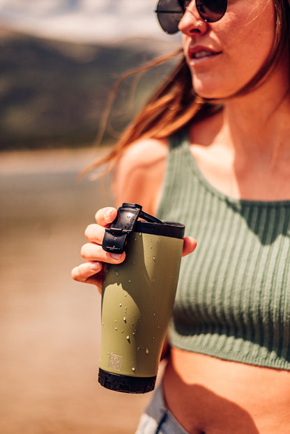 Woman holding a green coffee tumbler outdoors with a blurred natural background