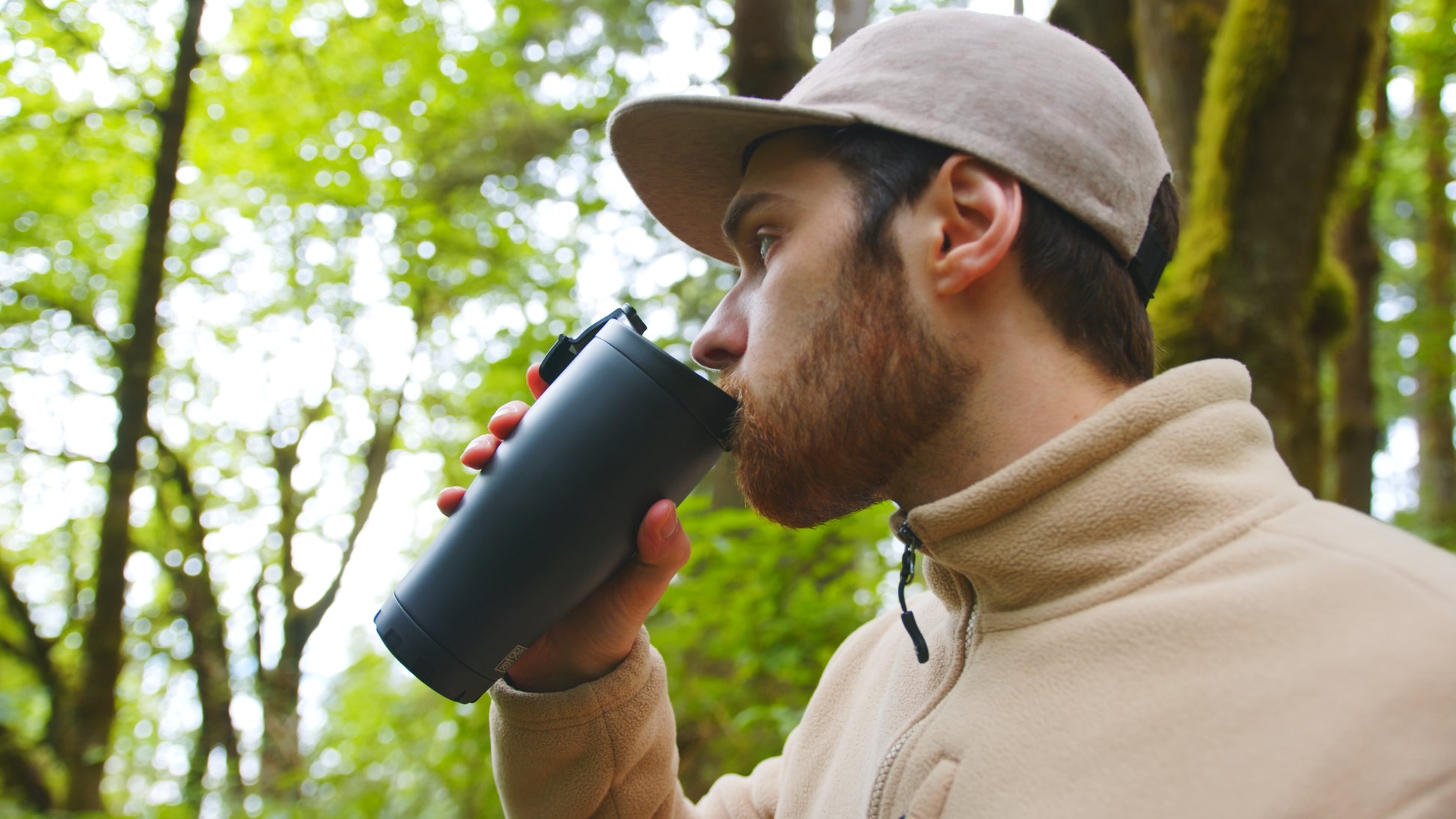 Man drinking from a insulated black coffee tumbler in a forest setting