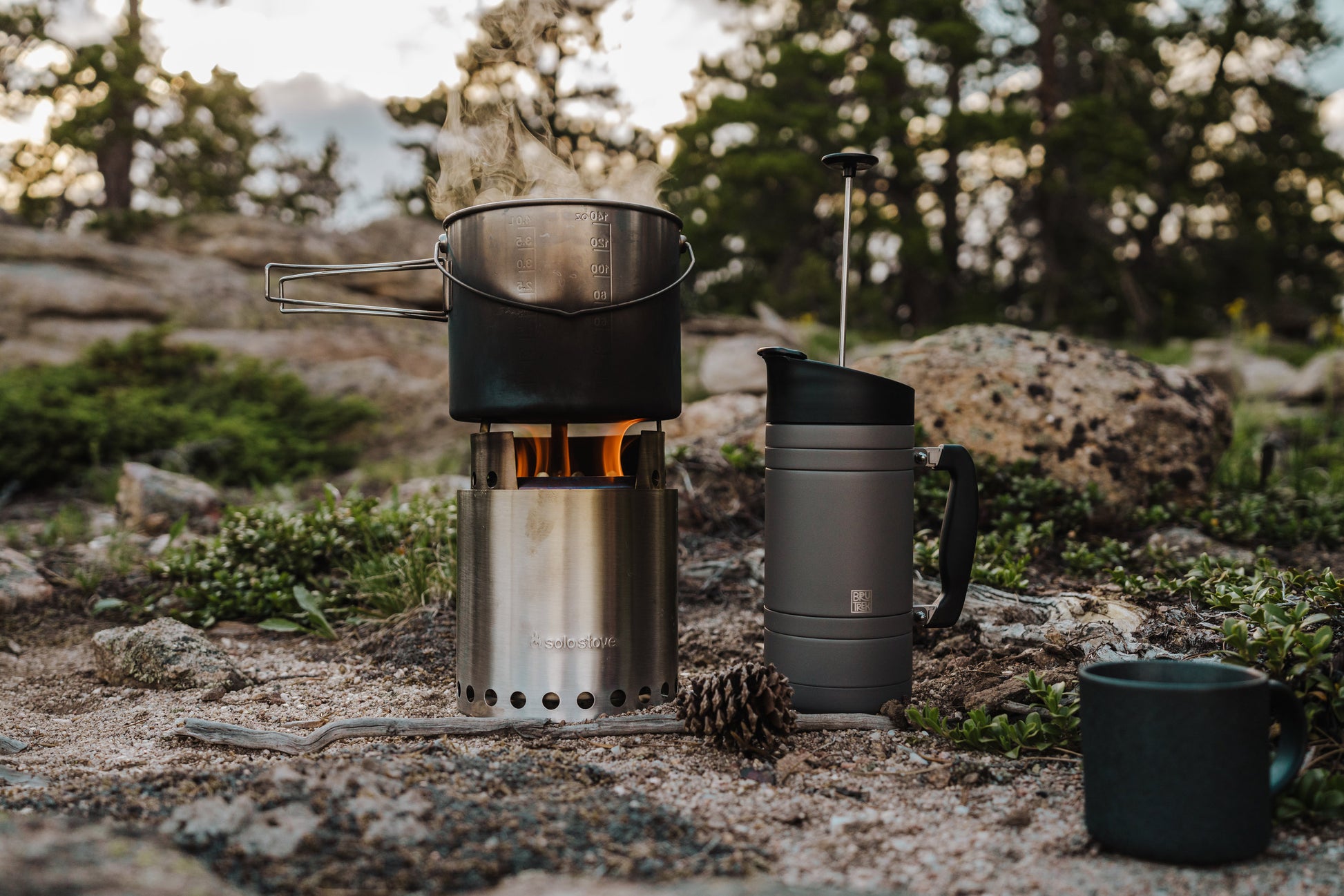 Camp stove with pot and insulated gray travel French Press on a natural outdoor setting
