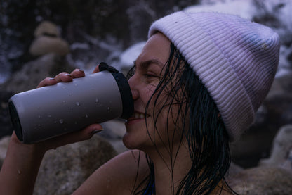 Person drinking from a insulated mug outdoors in a snowy setting