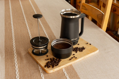 Coffee-making setup with a French press, coffee grounds, on a wooden board.
