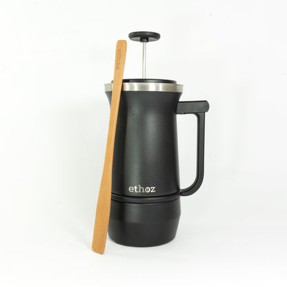Black French press coffee maker with a wooden stirrer on a white background