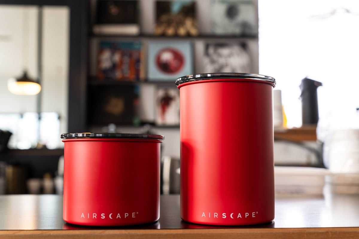 Two red Airscape canisters on a wooden surface with a blurred kitchen background