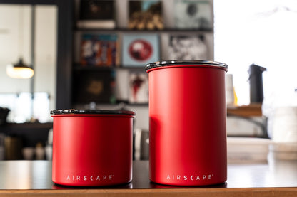 Two red Airscape canisters on a wooden surface with a blurred kitchen background
