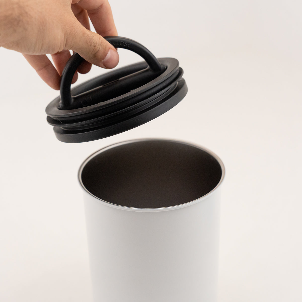 Hand opening a white container with a black lid on a light gray background