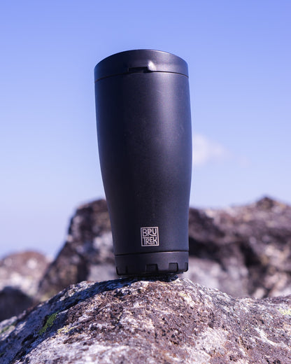 Black travel mug on a rock with a blurred natural background